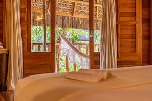 Una habitación de madera con cama, cortinas y una hamaca.