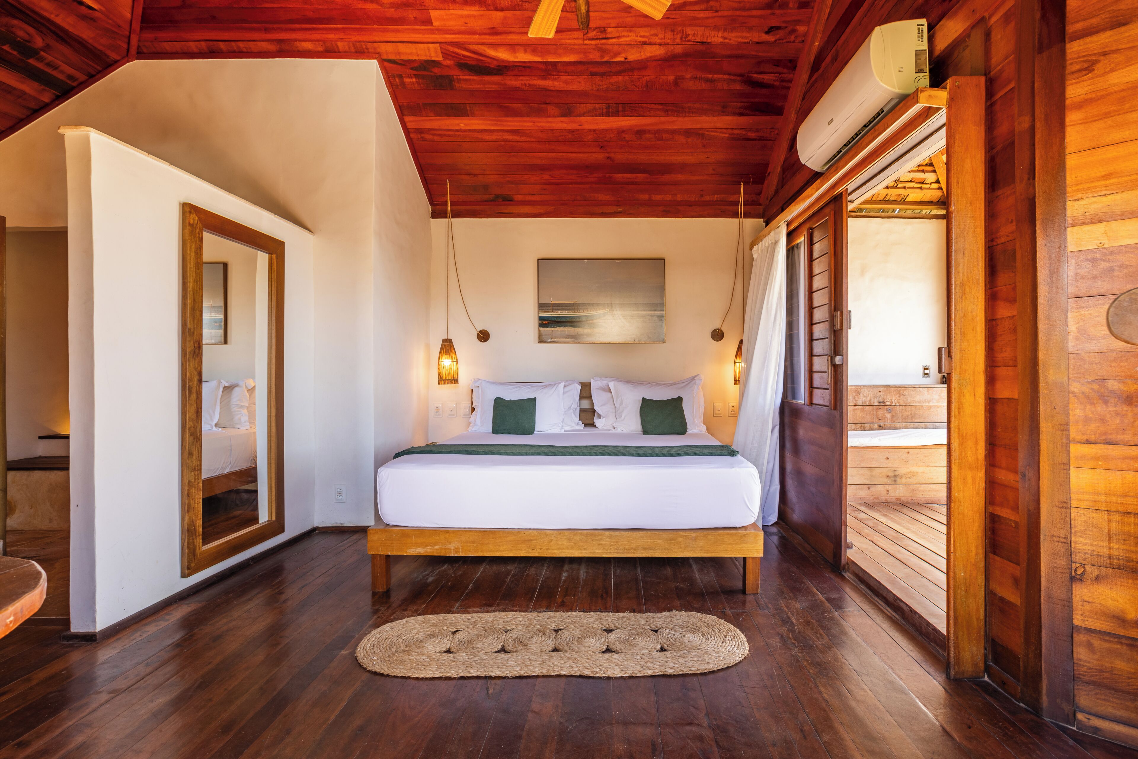 Una habitación con estructura de madera, una cama, un espejo y un ventilador de techo.