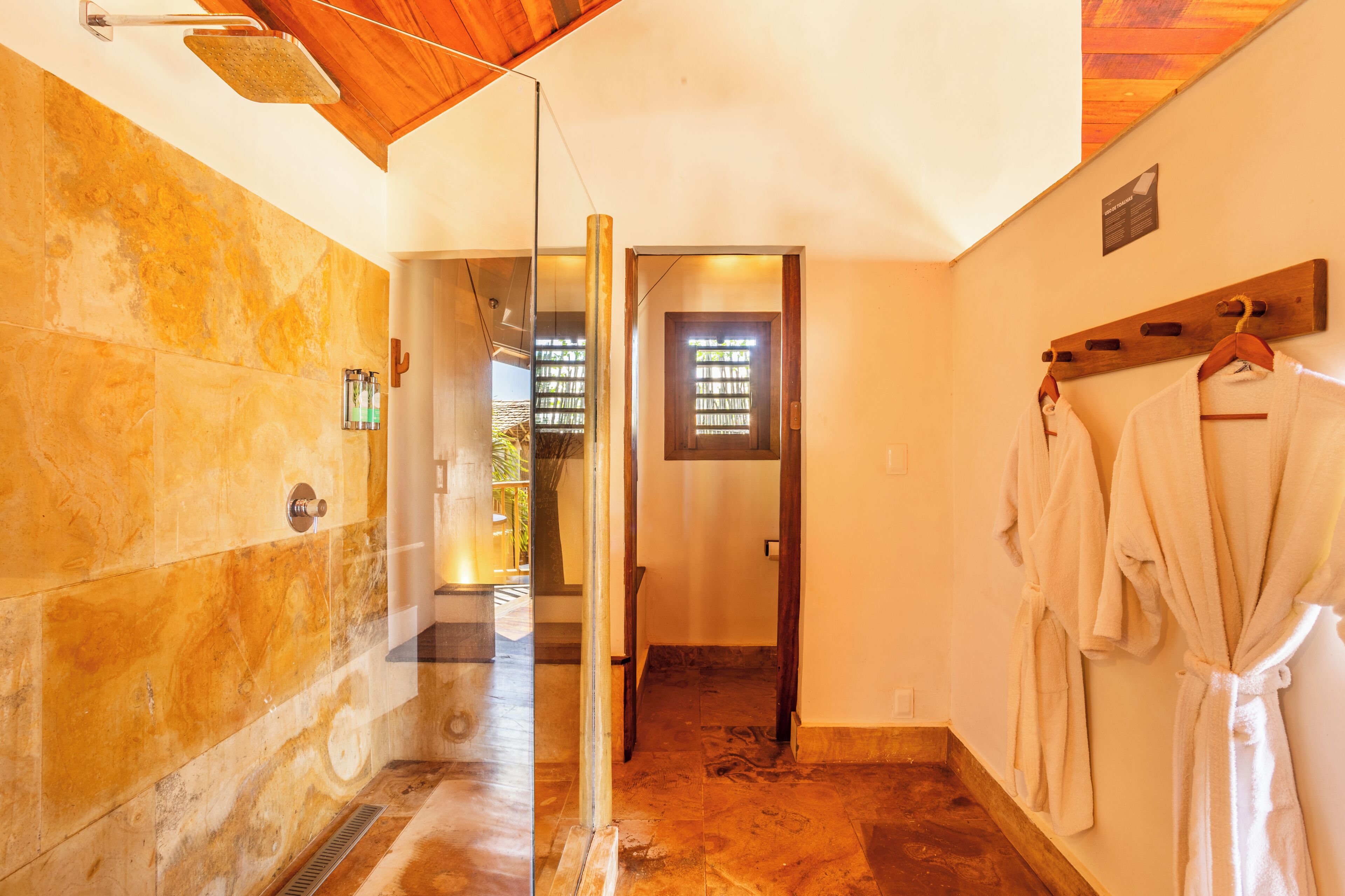 Uma casa de banho de hotel com cabine de duche em vidro, teto de madeira e um porta-toalhas.