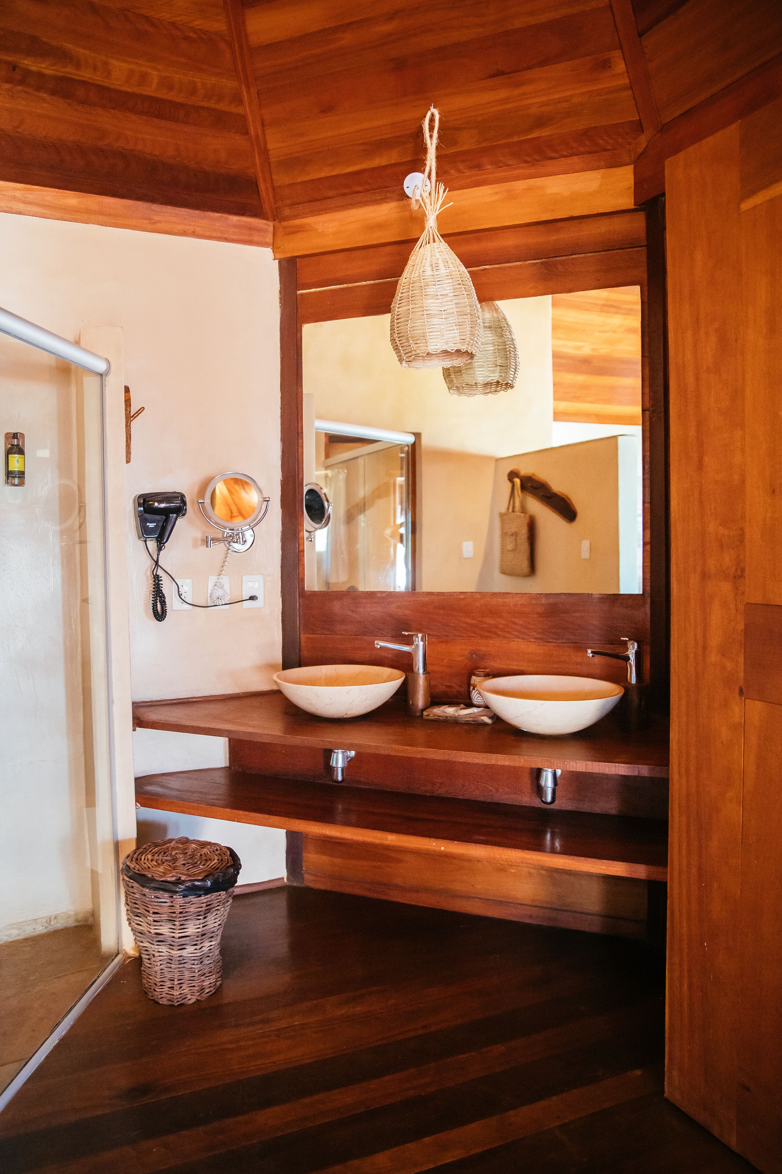 A wooden bathroom with two sinks, a mirror, and a hanging light fixture.