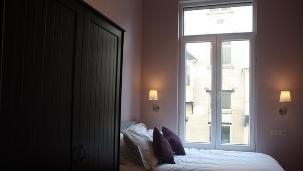 A bedroom with a bed, a wardrobe, and two wall-mounted lamps. - Eu B&B (Brussels)