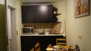 A compact kitchen with dark cabinets, a microwave, a coffee maker, and a dining table set with breakfast items. - Eu B&B (Brussels)