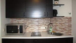 A kitchen with dark cabinets, a microwave, a sink, and a tiled backsplash. - Eu B&B (Brussels)