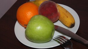 A plate with a green apple, an orange, a peach, and a banana. - Eu B&B (Brussels)