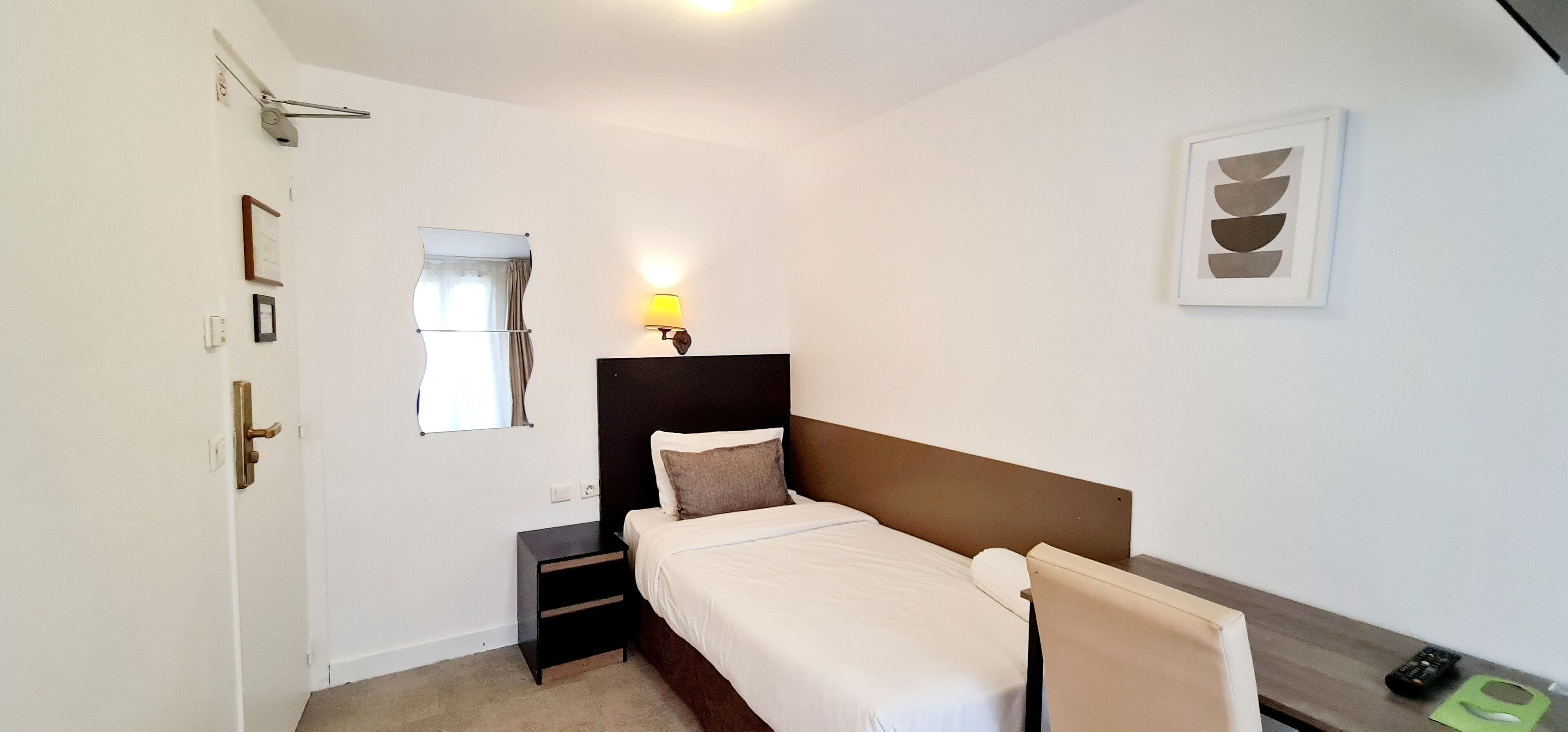 Una habitación de hotel con cama, mesita de noche, lámpara y un cuadro en la pared.