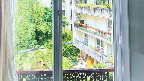 A view from a balcony with a metal railing, overlooking a multi-story building with balconies, greenery, and a clear sky. - Hotel de France (Paris)
