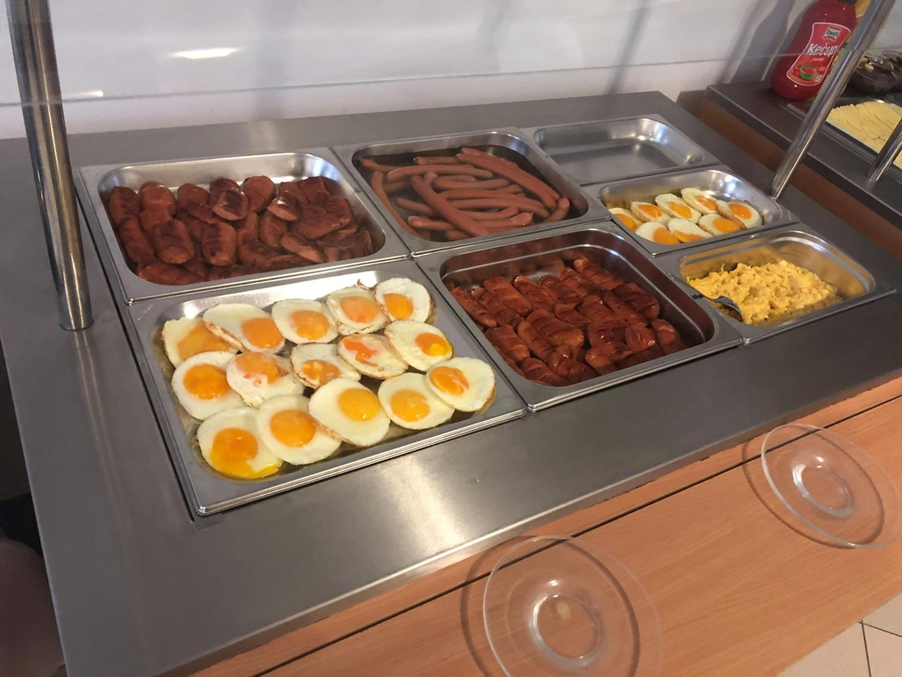 Un bufé con diversas opciones de comida, incluyendo salchichas, huevos y huevos revueltos.