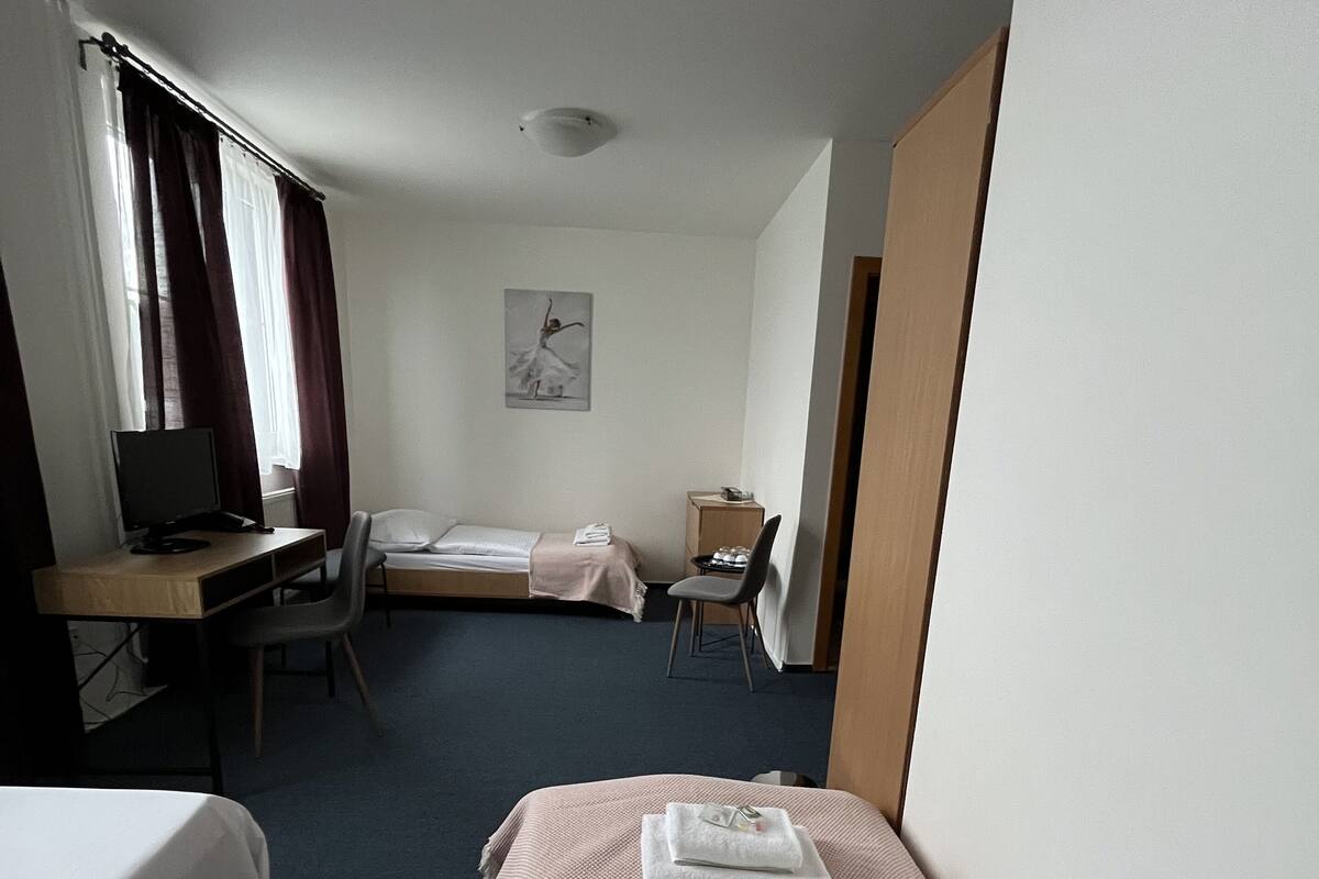A hotel room with two single beds, a desk with a computer, a chair, and a small table.