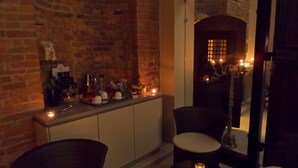Una habitación acogedora con pared de ladrillo, un mueble de madera y dos sillas. Velas sobre el mueble y las sillas.