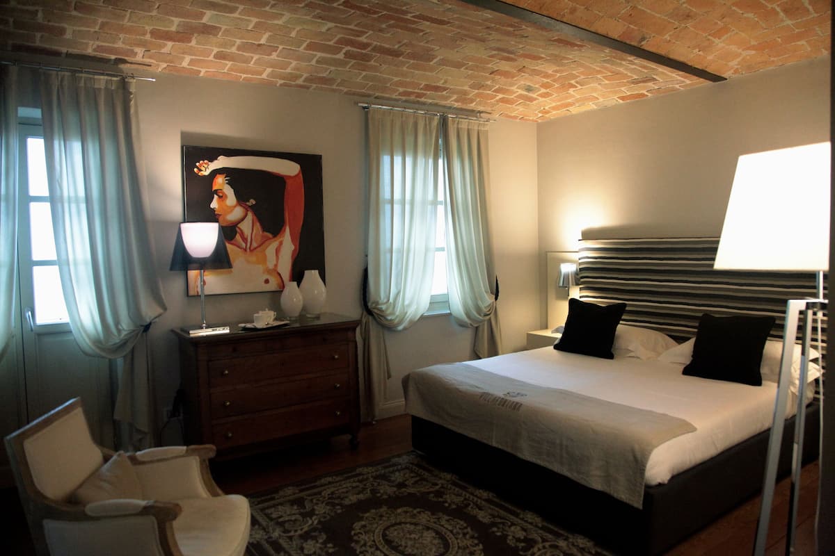 Een slaapkamer met een bed, een kaptafel, een stoel, een schilderij en een raam met gordijnen.