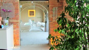 Vista del interior de un vestíbulo de hotel con pared de ladrillo, un mostrador de recepción y un amplio arco que da a una habitación.