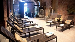 Zona de spa con sillones de mimbre, una silla colgante y una pared de ladrillo.