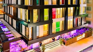 Een meerhoog hotel met verlichte ramen en een goed verlicht buitengebied met zitplaatsen en planten.