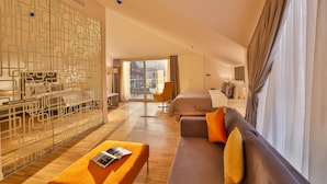Een moderne hotelkamer met een houten vloer, een bank met oranje kussens, een bed, een glazen scheidingswand en een stadszicht door grote ramen.
