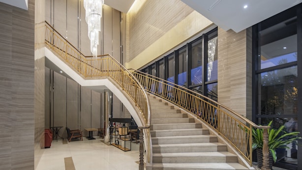 A grand staircase with a golden railing leading to an upper floor, surrounded by modern decor and large windows. - Holiday Inn Express Shanghai New Jinqiao by IHG (Shanghai)