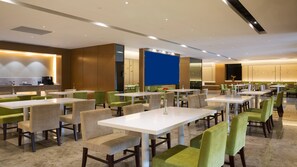 A modern dining area with multiple tables and chairs, a kitchen area, and a blue accent wall.