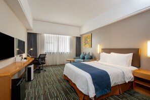 A hotel room with a bed, desk, chair, and TV.