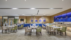 A spacious dining area with multiple tables and chairs, a buffet counter, and a large screen displaying food items. - Holiday Inn Express Shanghai New Jinqiao by IHG (Shanghai)