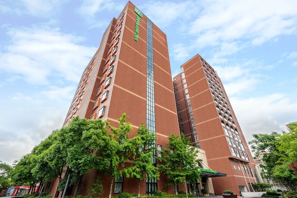 A high-rise building with multiple floors, featuring a prominent vertical strip of windows and a green sign at the top.