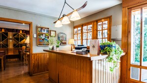 A wooden reception desk with a hanging light fixture, a plant, and a window with a view of greenery. - Hotel Esquirol (Llívia)