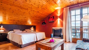A cozy room with wooden ceiling and walls, two beds, a small table with a flower, a chair, and a view of the outdoors through a large window. - Hotel Esquirol (Llívia)