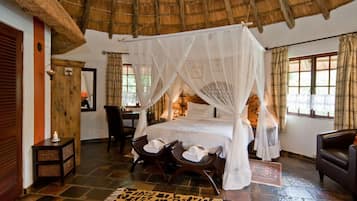 A room with a bed under a canopy, a desk with a chair, a mirror, and a window with curtains.