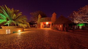 A nighttime view of a building with a brick entrance, a reception area, and a thatched-roof structure. - Aquanzi Lodge (Chartwell)