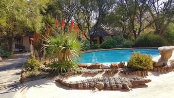A pool surrounded by tropical plants and a large stone sculpture.