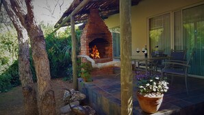A brick outdoor fireplace under a wooden pergola, surrounded by greenery and a stone wall. - Aquanzi Lodge (Chartwell)