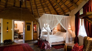 A room with a four-poster bed, a red patterned rug, and a thatched ceiling. - Aquanzi Lodge (Chartwell)