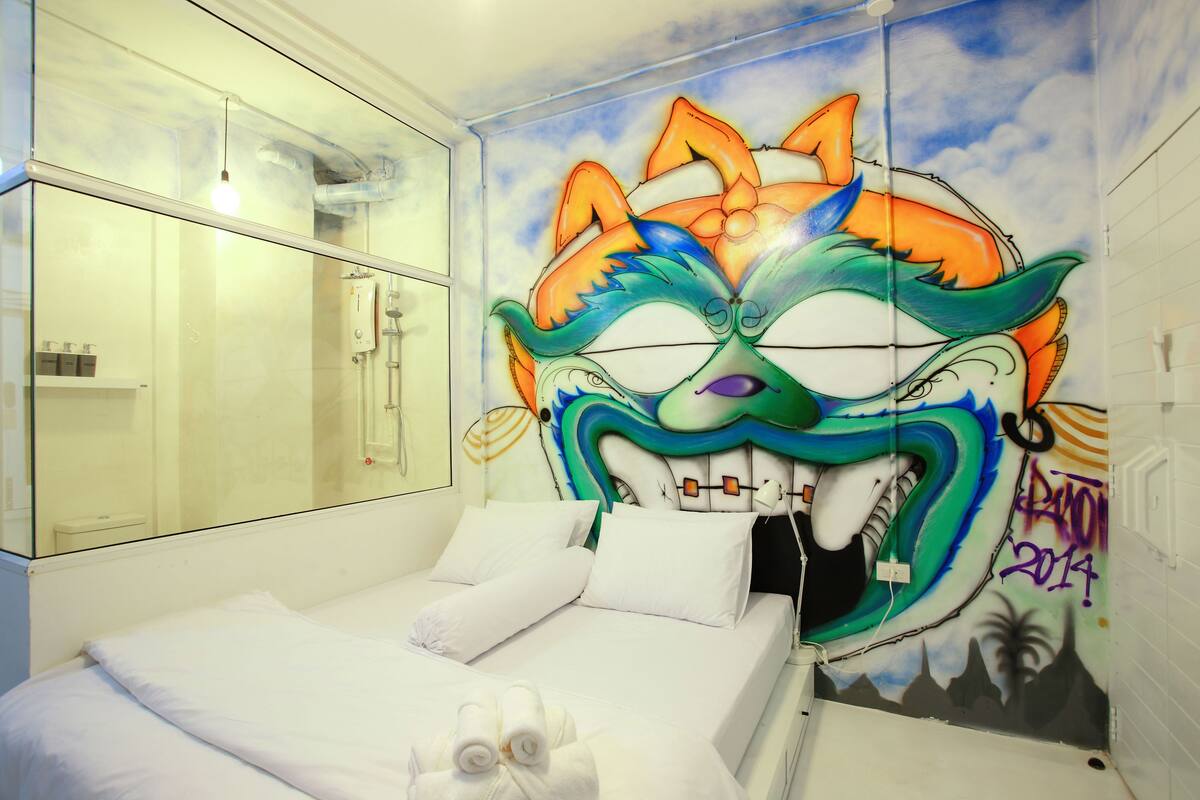 Habitación de hotel con cama, cabina de ducha de vidrio y un mural en la pared.