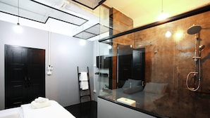 A modern hotel room with a large mirror, a glass shower enclosure, a bed with white linens, and a black wardrobe. - Meroom (Phuket)