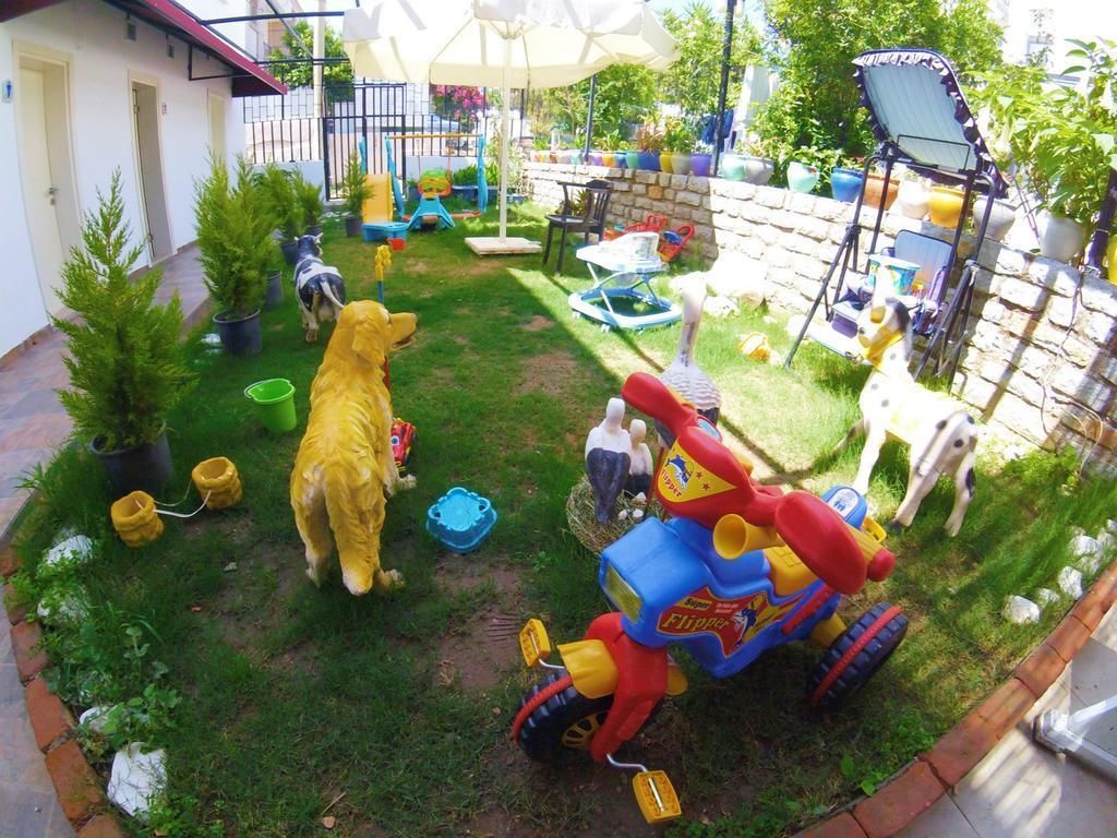 A fenced backyard with a lawn, a yellow dog, a small blue and red toy tractor, and various outdoor toys and furniture.