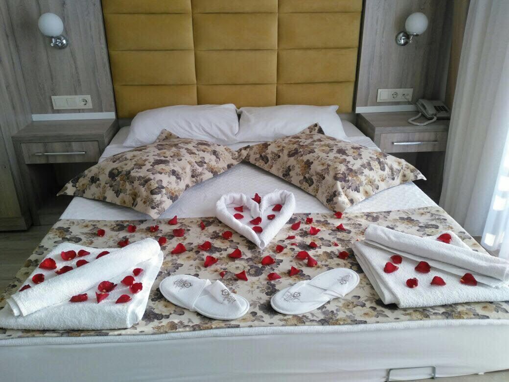 A neatly made bed with floral bedding, white towels, and slippers, and a bedside phone.