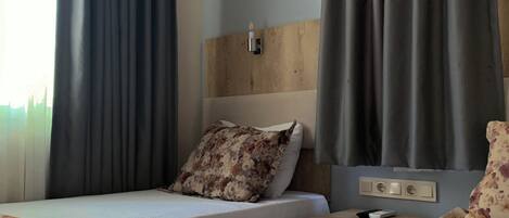Habitación de hotel con dos camas, cabecero de madera, mesita de noche con control remoto y colcha estampada con motivos florales.