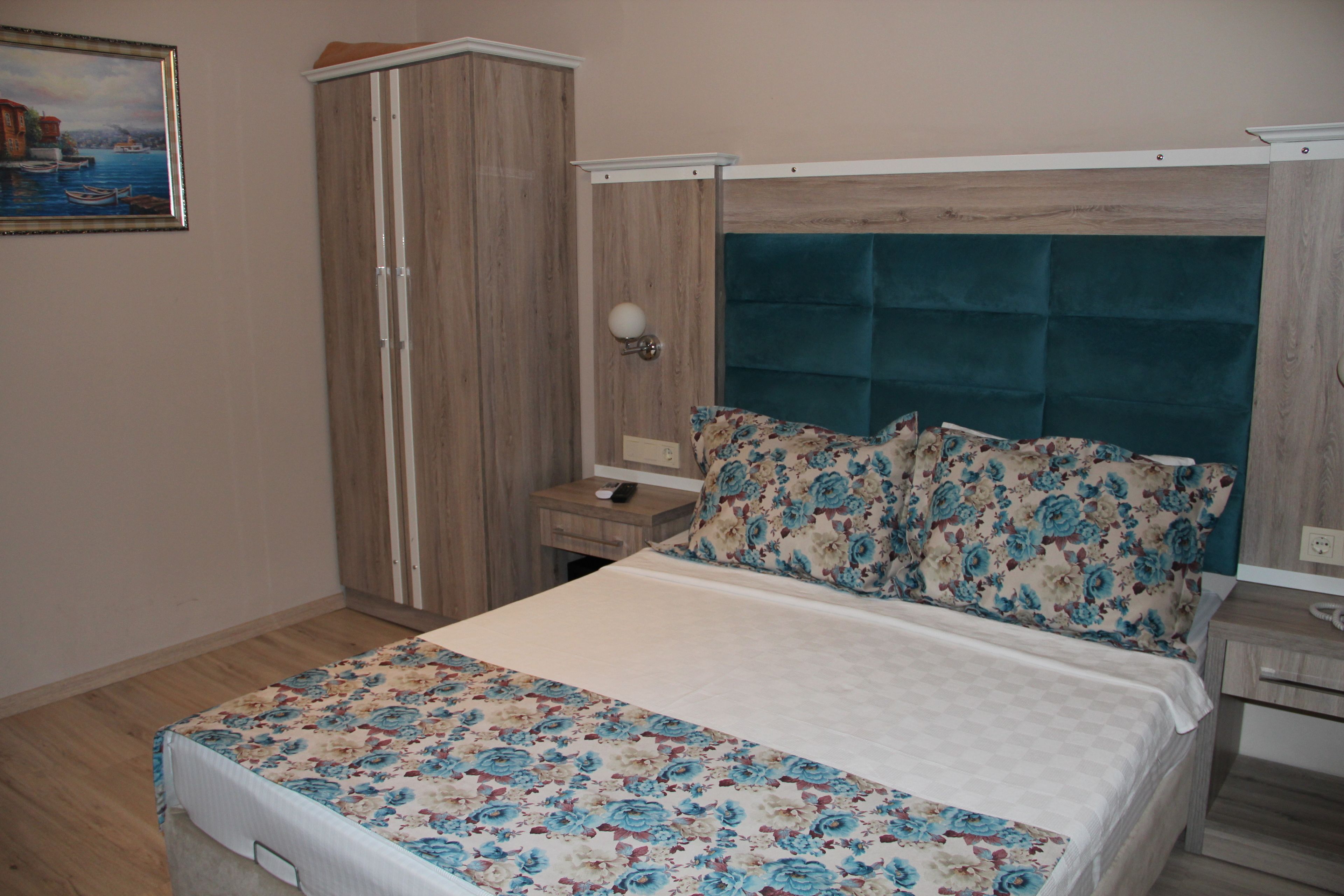 A bedroom with a bed, a nightstand, a wardrobe, and a wall-mounted lamp.