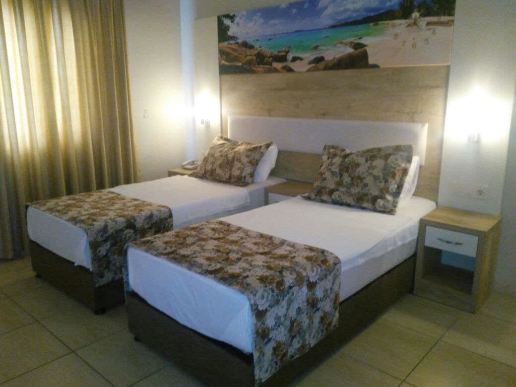 A hotel room with two beds, each with a floral bedspread, a nightstand with a lamp, and a painting of a beach scene on the wall.