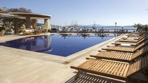 A pool area with lounge chairs, a gazebo, and boats in the background. - Akkan Beach Hotel (Bodrum)