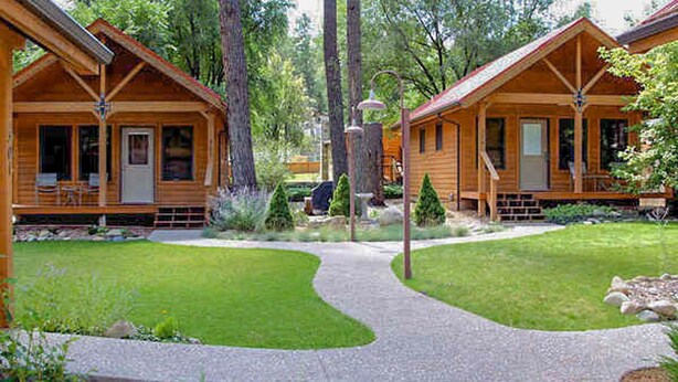A wooden cabin-style lodging with a central walkway, surrounded by lush greenery and trees. - Shadow Mountain Lodge and Cabins (Ruidoso)