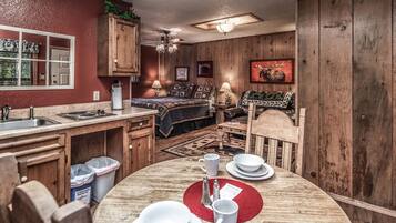 A compact kitchen with wooden cabinets, a dining table set with white plates and cups, and a ceiling fan.