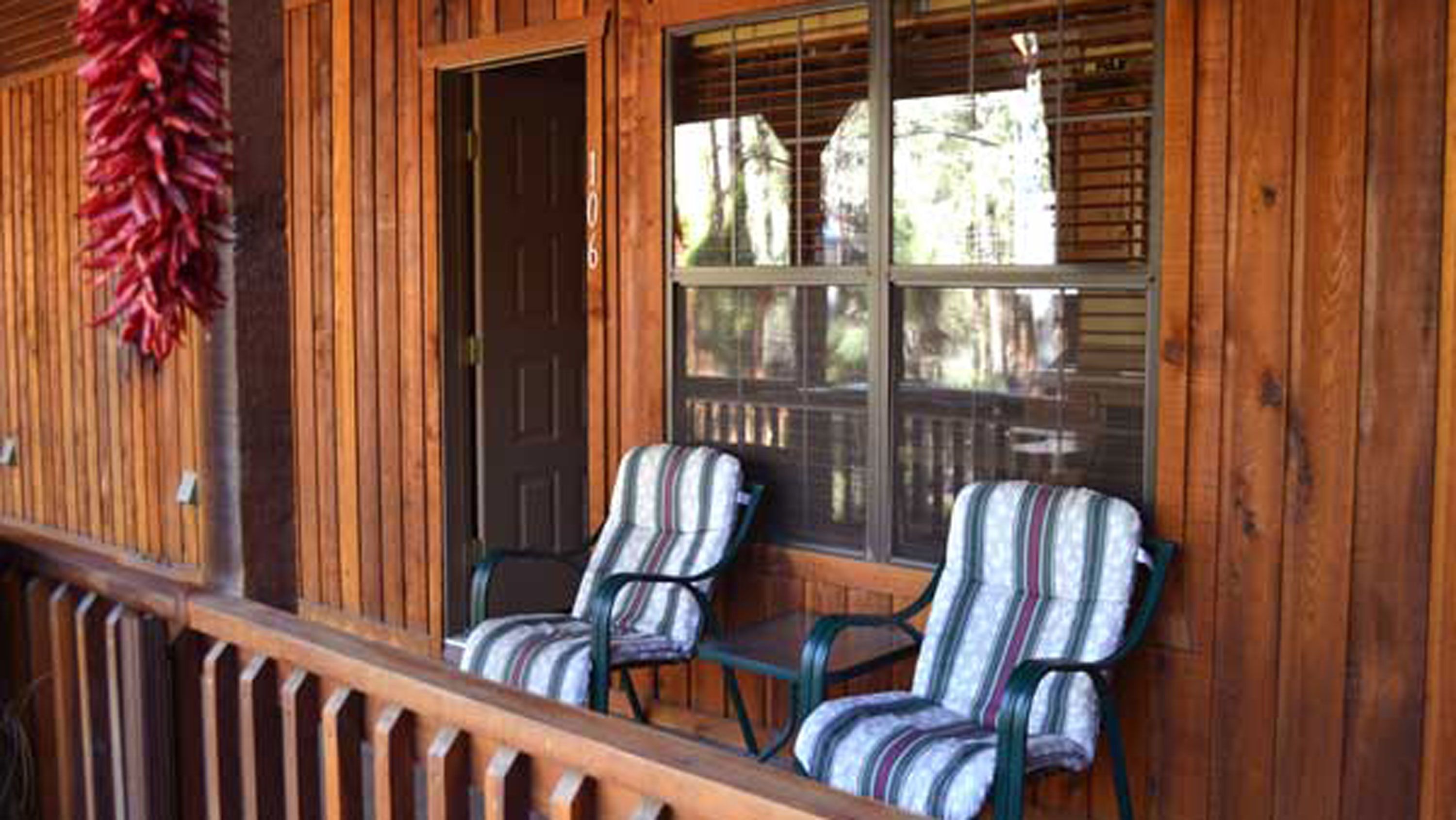 A wooden porch with two striped chairs and a door.