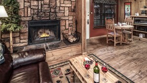 A cozy living room with a stone fireplace, wooden furniture, and a dining area with a table and chairs. - Shadow Mountain Lodge and Cabins (Ruidoso)