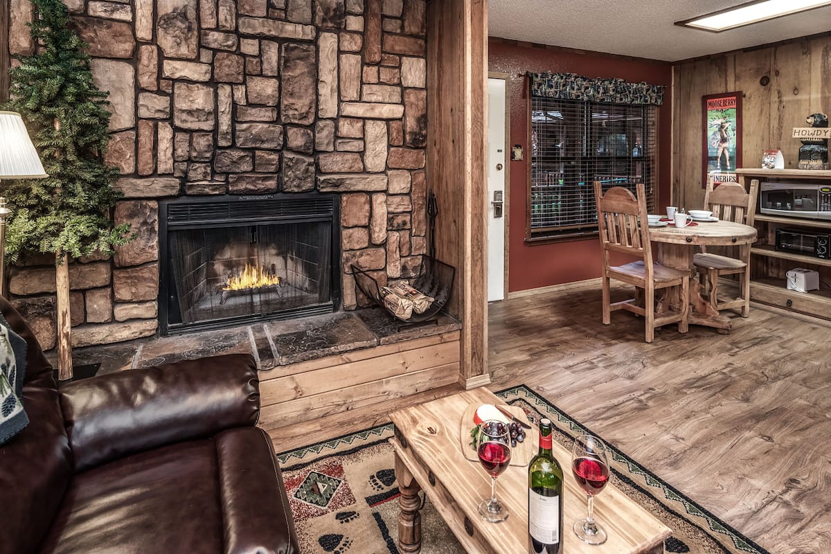 A cozy living room with a stone fireplace, wooden furniture, and a dining area with a table and chairs.