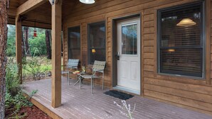 A wooden cabin with a porch, two chairs, a table, and a hanging light fixture. - Shadow Mountain Lodge and Cabins (Ruidoso)