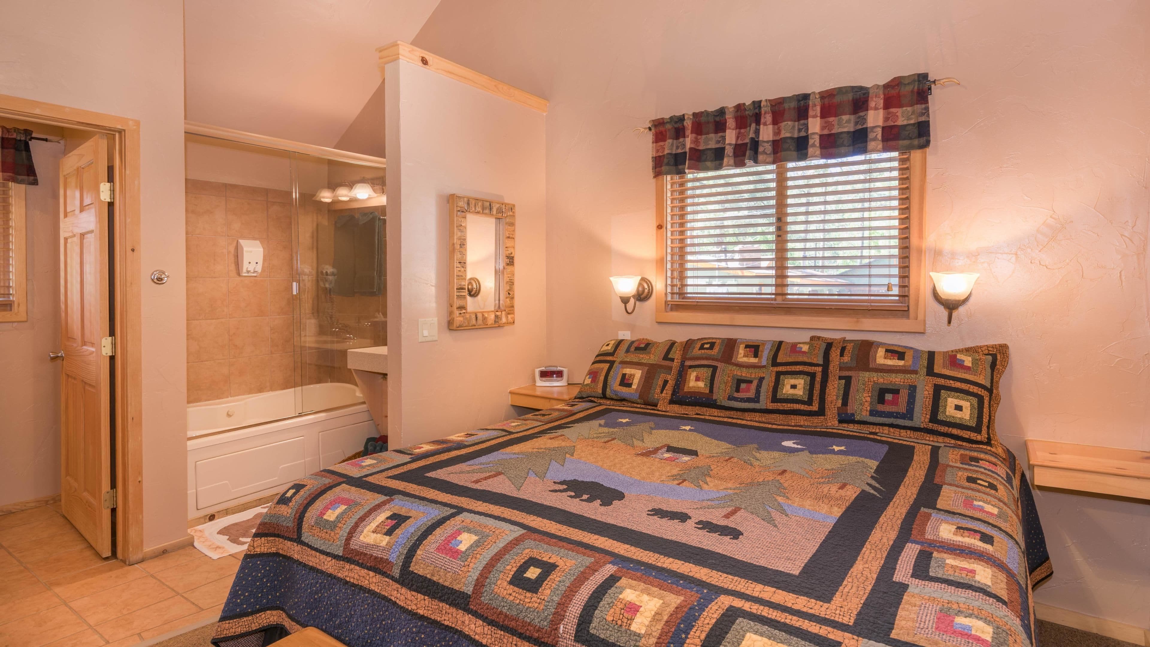 Un dormitorio con una cama grande, una ventana con persianas, una mesita de noche, un espejo, una puerta y un baño con ducha e inodoro.