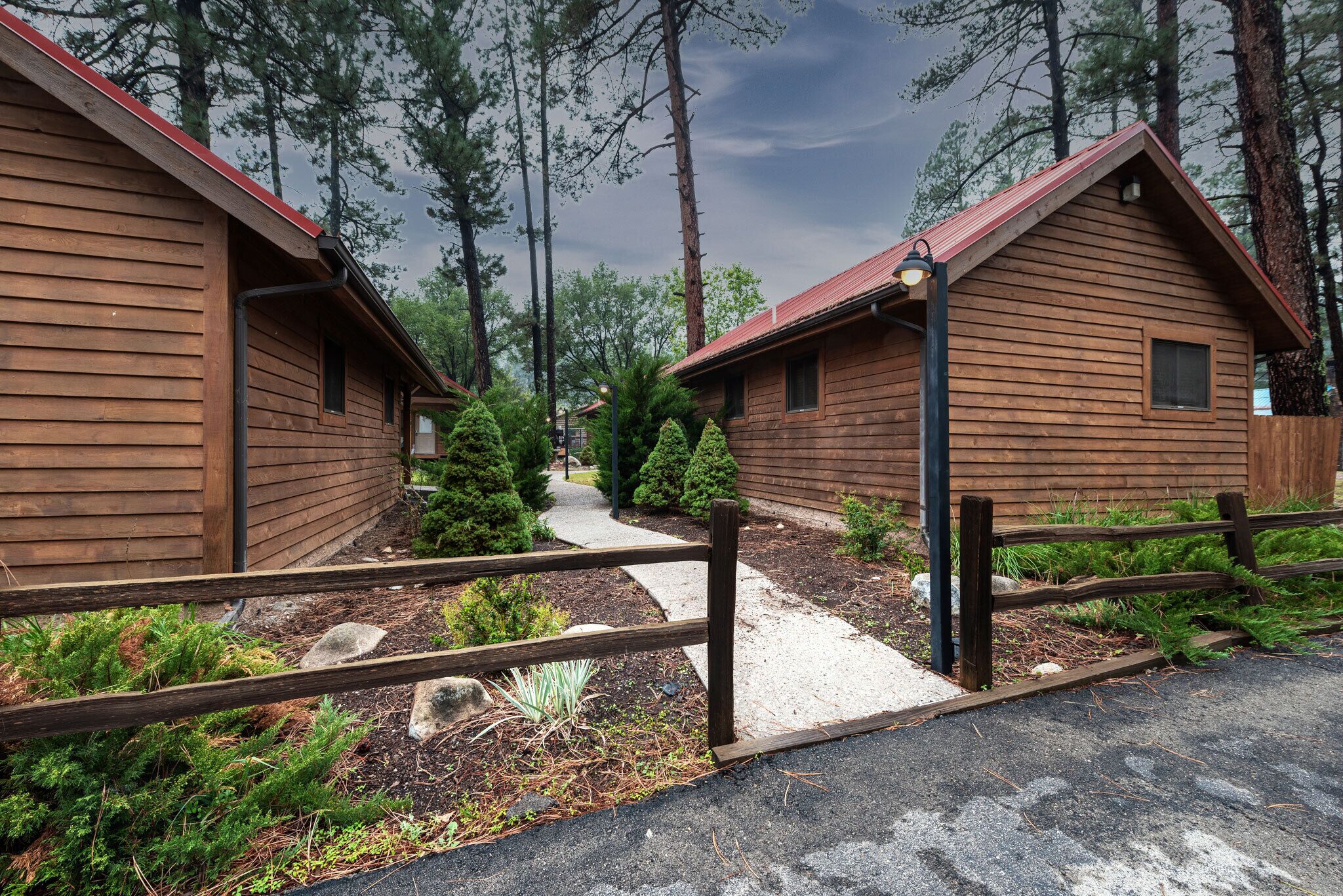 A row of wooden cabins with a gravel path leading to them, surrounded by trees.