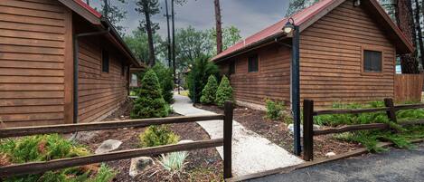 A row of wooden cabins with a gravel path leading to them, surrounded by trees.