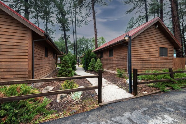 A row of wooden cabins with a gravel path leading to them, surrounded by trees. - Shadow Mountain Lodge and Cabins (Ruidoso)