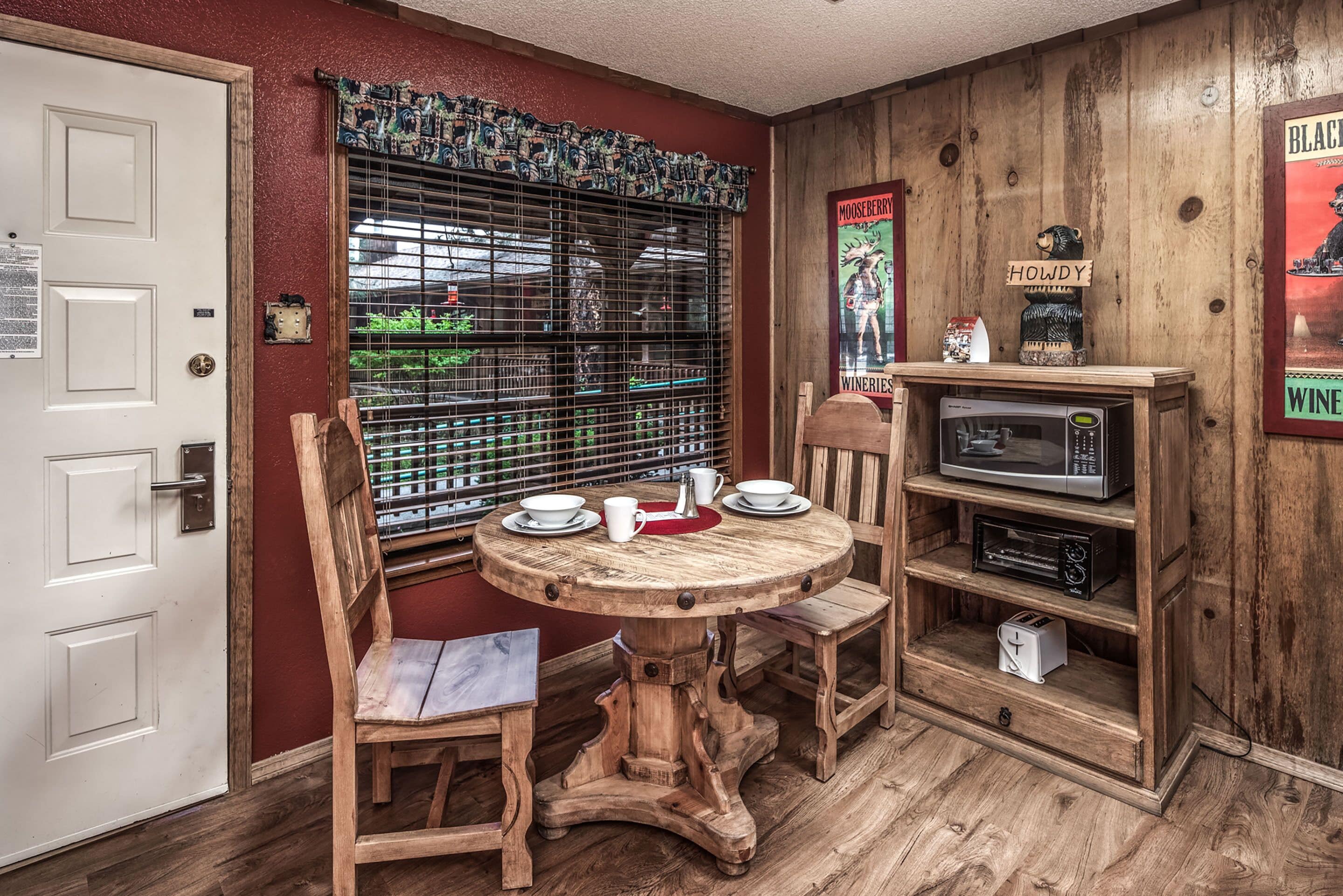 Una mesa de comedor de madera con sillas, un microondas y una estantería con un tostador.