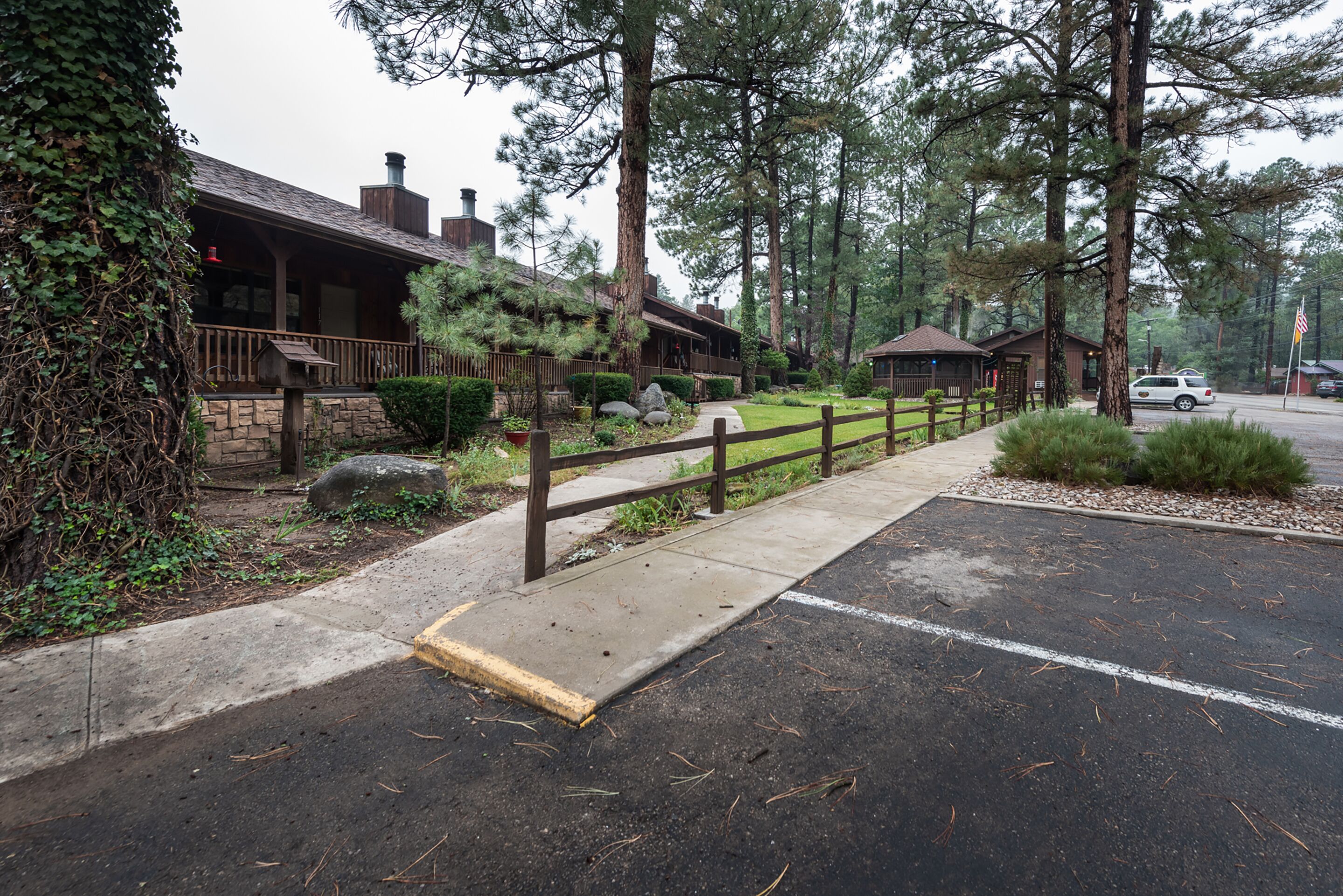 A rustic lodge with a stone facade, wooden deck, and a fenced parking area.
